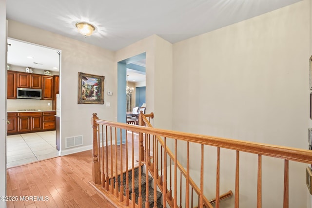 hallway featuring visible vents, an upstairs landing, baseboards, and light wood-style flooring