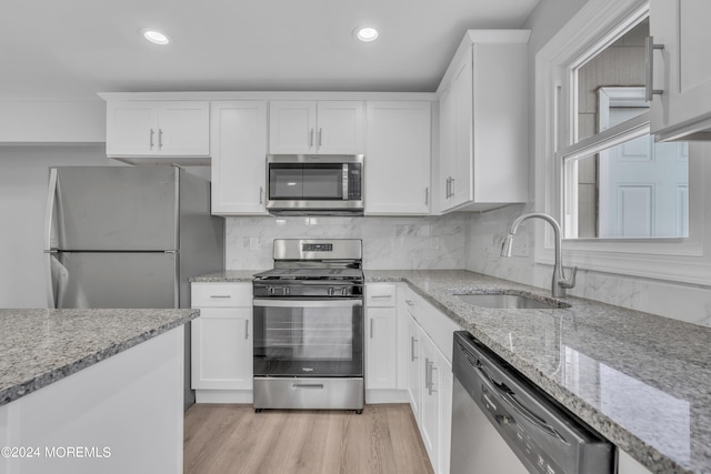 kitchen with appliances with stainless steel finishes, white cabinets, a sink, and light wood-style flooring