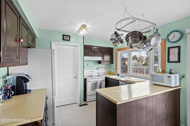 kitchen with dark brown cabinetry, under cabinet range hood, white appliances, a sink, and light countertops