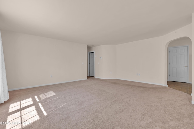 unfurnished room with baseboards, arched walkways, and carpet