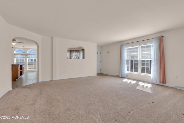 unfurnished living room featuring a wealth of natural light, arched walkways, and carpet flooring