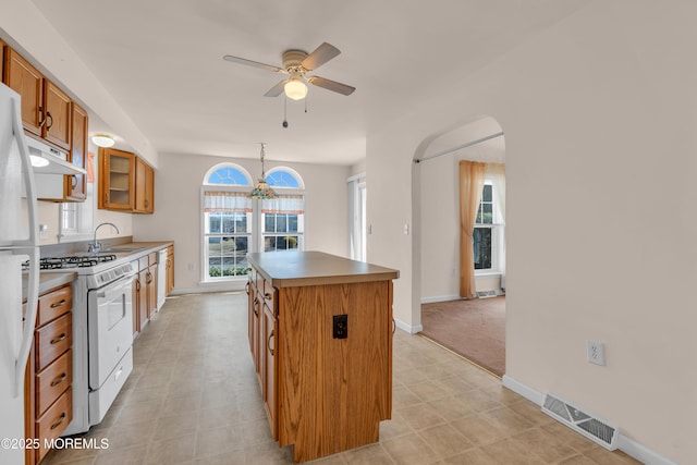 kitchen with white appliances, visible vents, a kitchen island, a sink, and brown cabinets