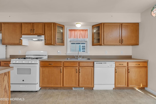 kitchen featuring glass insert cabinets, under cabinet range hood, brown cabinets, white appliances, and a sink