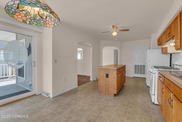 kitchen featuring visible vents, white range with gas cooktop, arched walkways, under cabinet range hood, and a center island