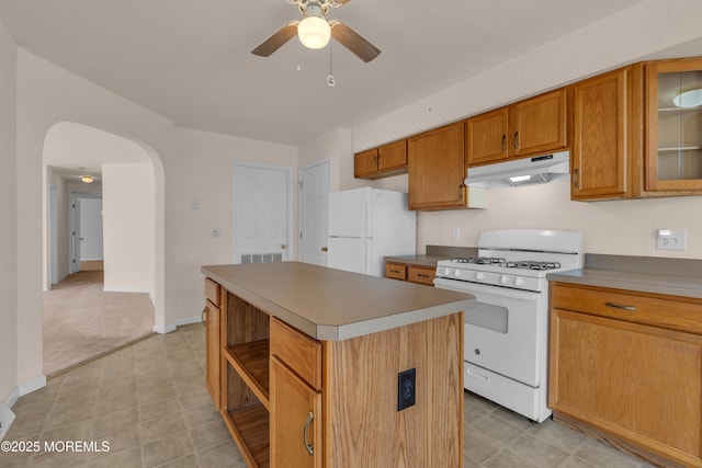 kitchen with under cabinet range hood, a center island, white appliances, arched walkways, and brown cabinetry