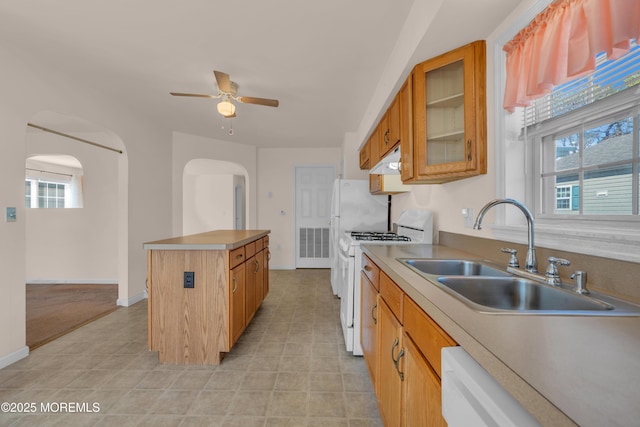 kitchen featuring a sink, white appliances, a kitchen island, and arched walkways