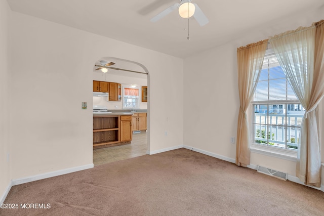 unfurnished living room with a wealth of natural light, visible vents, light colored carpet, and ceiling fan