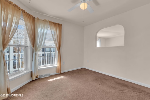 carpeted empty room featuring arched walkways, visible vents, a ceiling fan, and baseboards