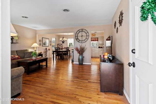 foyer entrance with a notable chandelier, light wood-type flooring, visible vents, and baseboards