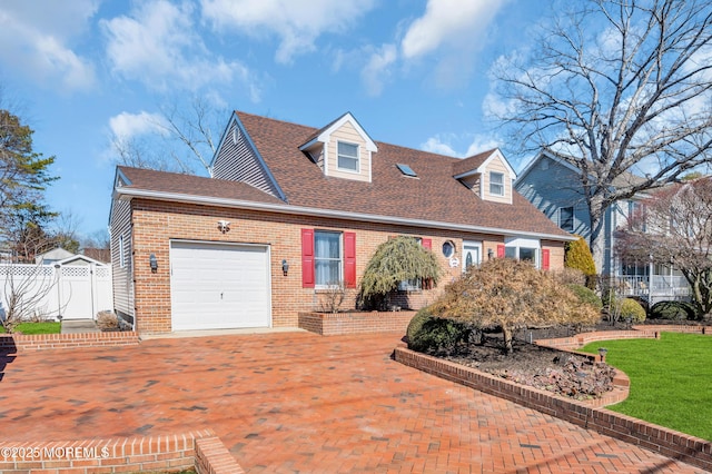 cape cod house featuring a garage, brick siding, fence, roof with shingles, and decorative driveway