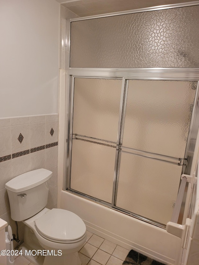 full bath with combined bath / shower with glass door, tile patterned flooring, toilet, and tile walls