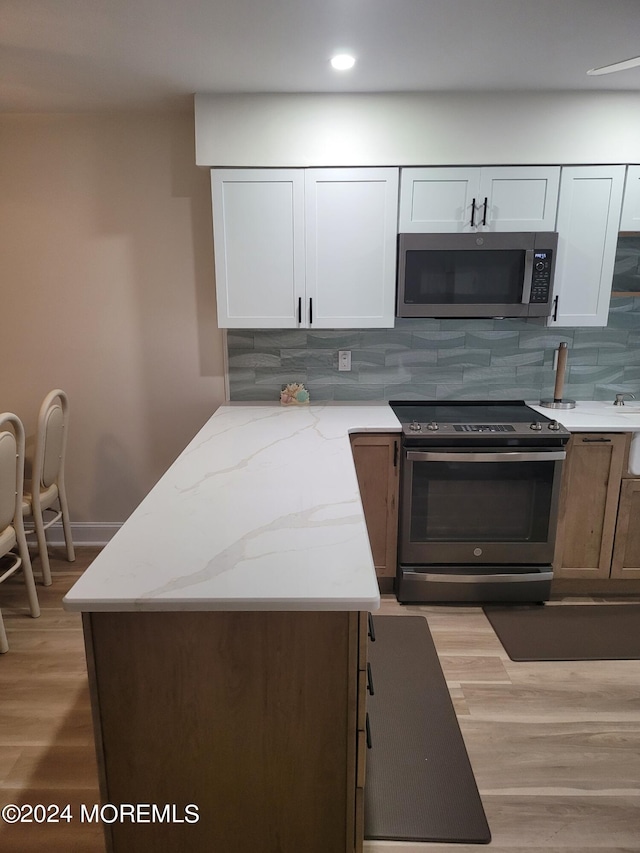 kitchen featuring light wood finished floors, appliances with stainless steel finishes, light stone countertops, and tasteful backsplash