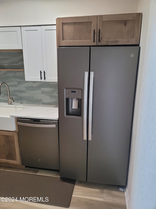 kitchen featuring tasteful backsplash, appliances with stainless steel finishes, light stone countertops, white cabinetry, and a sink