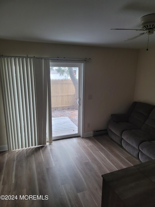 unfurnished living room featuring a baseboard radiator, baseboards, ceiling fan, and wood finished floors