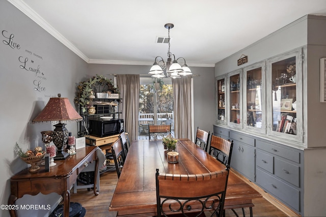 dining area with a chandelier, crown molding, and wood finished floors