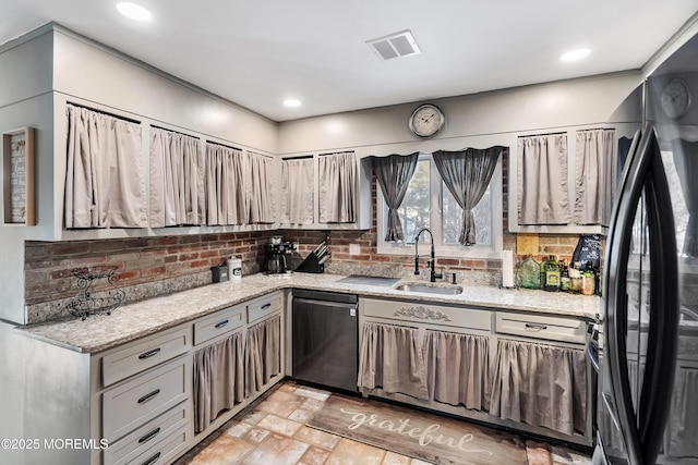 kitchen featuring dishwashing machine, a sink, visible vents, freestanding refrigerator, and tasteful backsplash