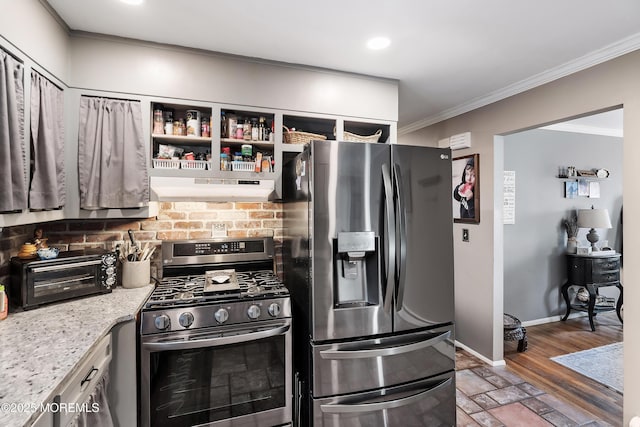 kitchen featuring a toaster, under cabinet range hood, baseboards, appliances with stainless steel finishes, and crown molding