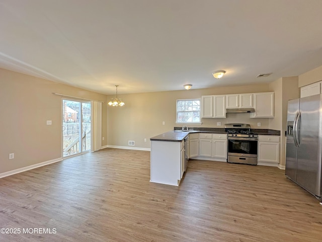 kitchen featuring light wood-style floors, dark countertops, appliances with stainless steel finishes, a peninsula, and under cabinet range hood