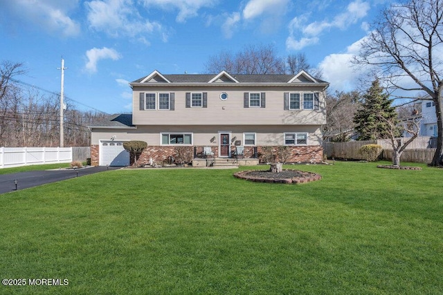 colonial house featuring aphalt driveway, a garage, a front lawn, and fence