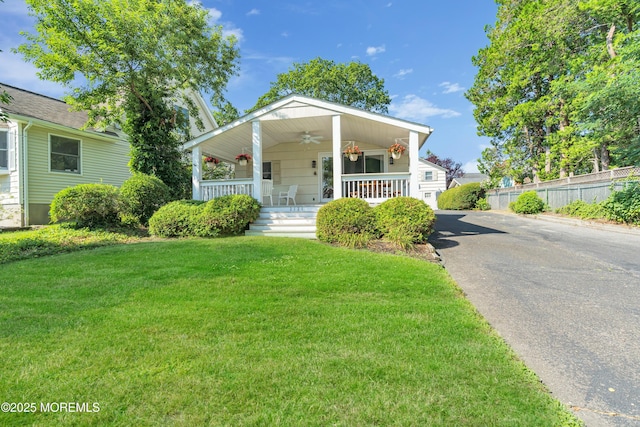 view of front of home featuring a porch, ceiling fan, fence, driveway, and a front lawn