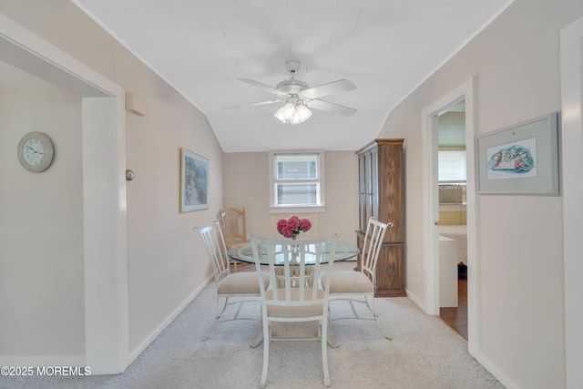 dining space with a ceiling fan, light colored carpet, vaulted ceiling, and baseboards