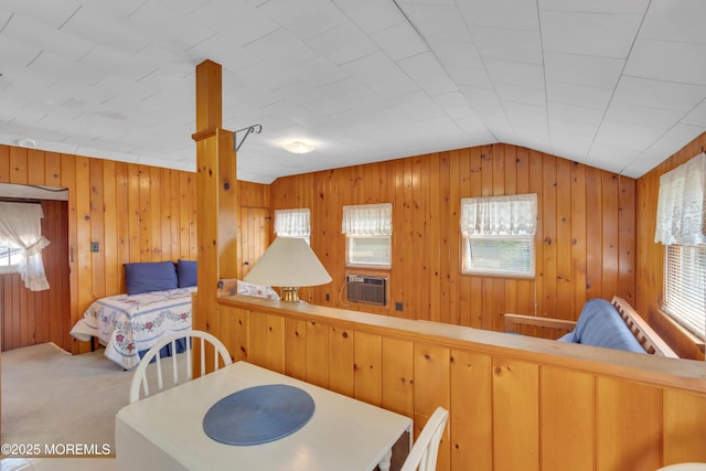 carpeted dining area featuring lofted ceiling, cooling unit, and wood walls