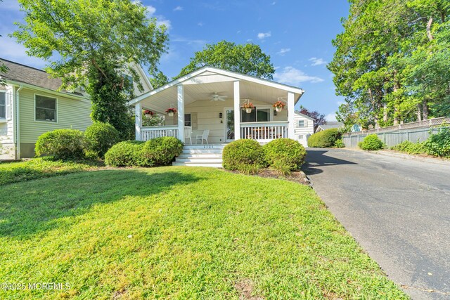 view of front of house with aphalt driveway, covered porch, a front yard, ceiling fan, and fence