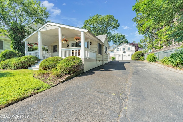 exterior space with covered porch, fence, an outdoor structure, driveway, and a front lawn