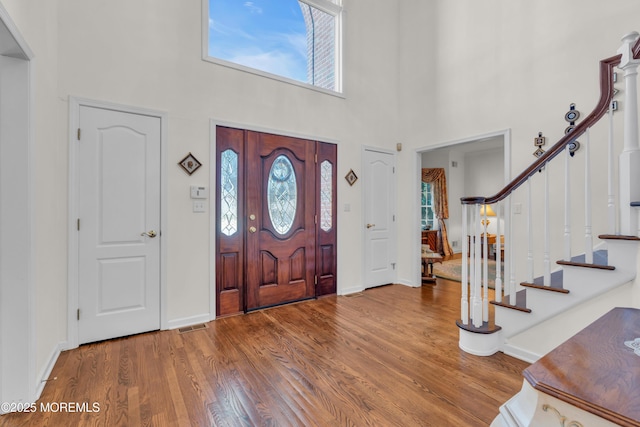 entrance foyer with stairway, a high ceiling, visible vents, and wood finished floors