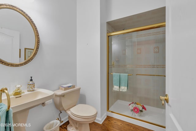 bathroom featuring toilet, wood finished floors, a stall shower, and baseboards