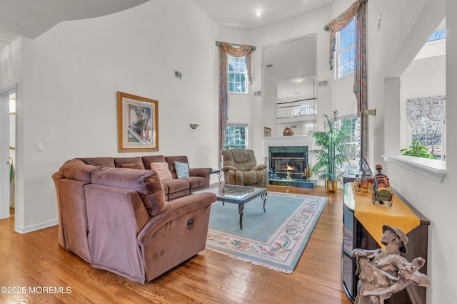 living area with wood finished floors, baseboards, visible vents, a premium fireplace, and a towering ceiling