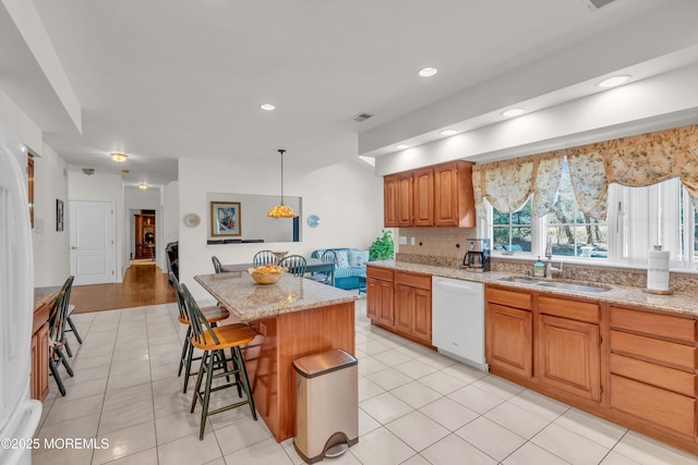 kitchen with visible vents, a sink, a kitchen island, a breakfast bar area, and white dishwasher