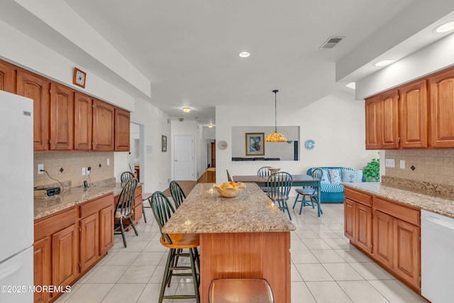 kitchen featuring light tile patterned floors, visible vents, white appliances, and a kitchen bar