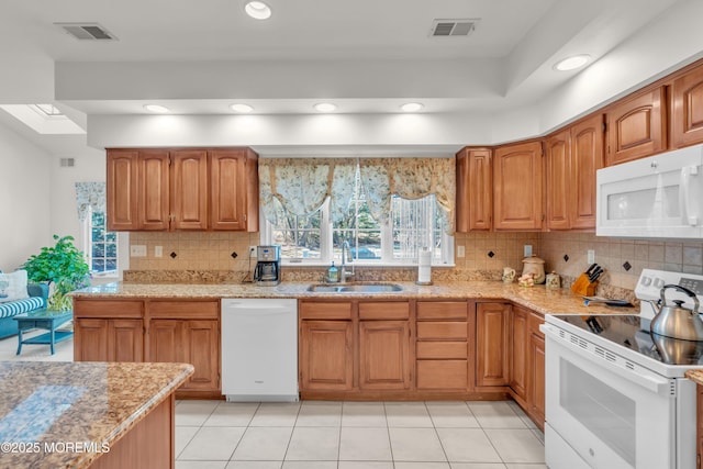 kitchen featuring white appliances, light stone counters, visible vents, and a sink