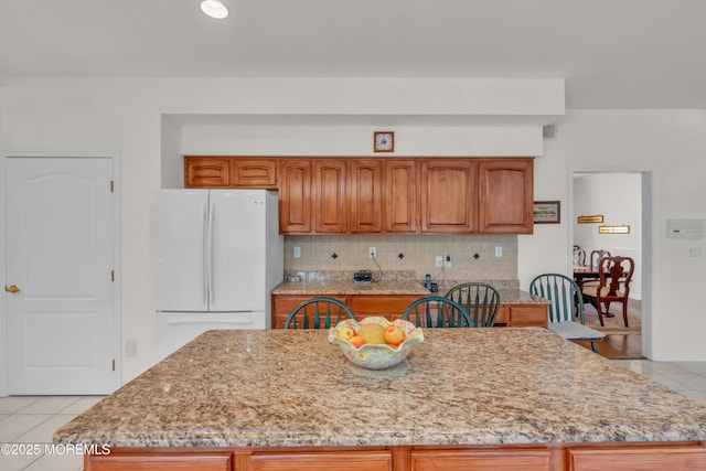 kitchen with decorative backsplash, light tile patterned floors, light stone countertops, and freestanding refrigerator