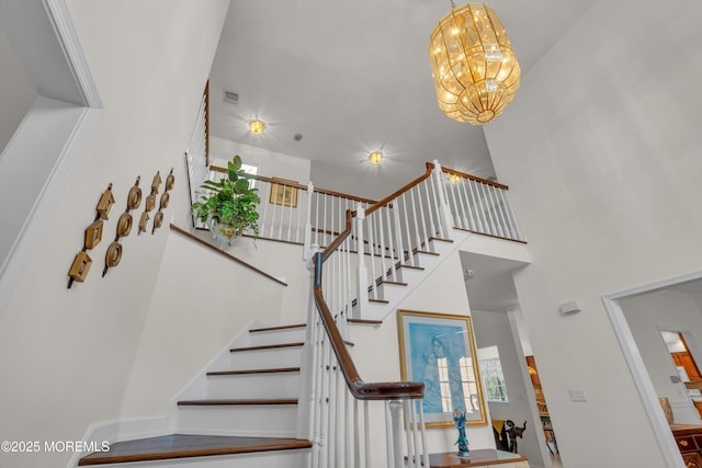 staircase featuring visible vents, a high ceiling, and a chandelier