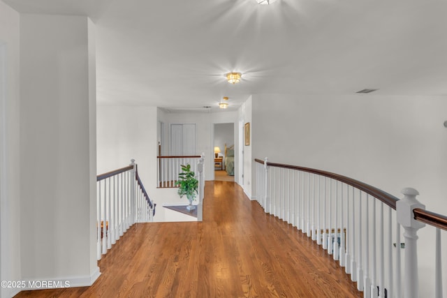 hall featuring wood finished floors, an upstairs landing, and visible vents