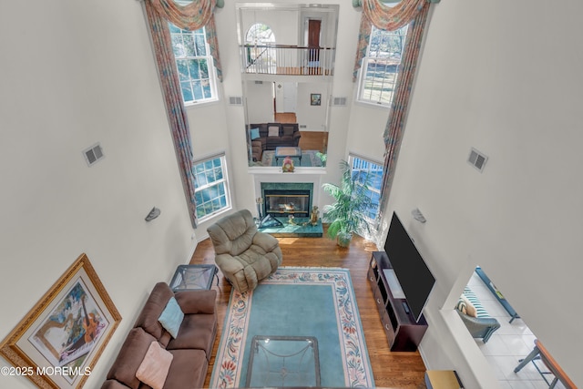 living room featuring a premium fireplace, visible vents, a high ceiling, and wood finished floors