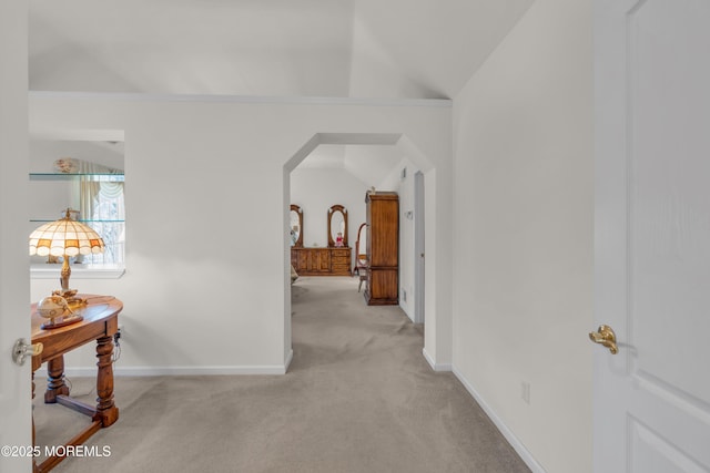 hall with lofted ceiling, light colored carpet, baseboards, and arched walkways