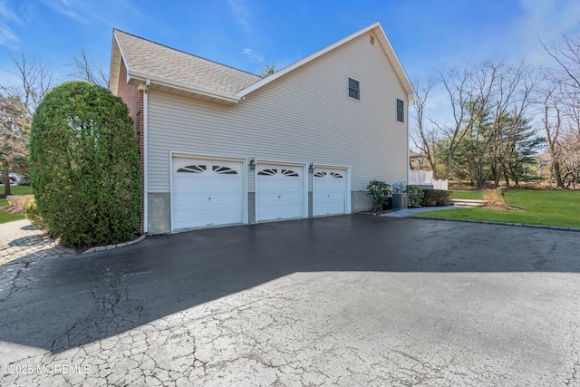 view of side of home featuring aphalt driveway, a garage, central AC unit, and roof with shingles