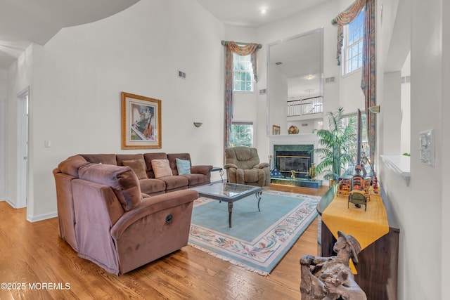 living area featuring a high end fireplace, visible vents, baseboards, a high ceiling, and wood finished floors