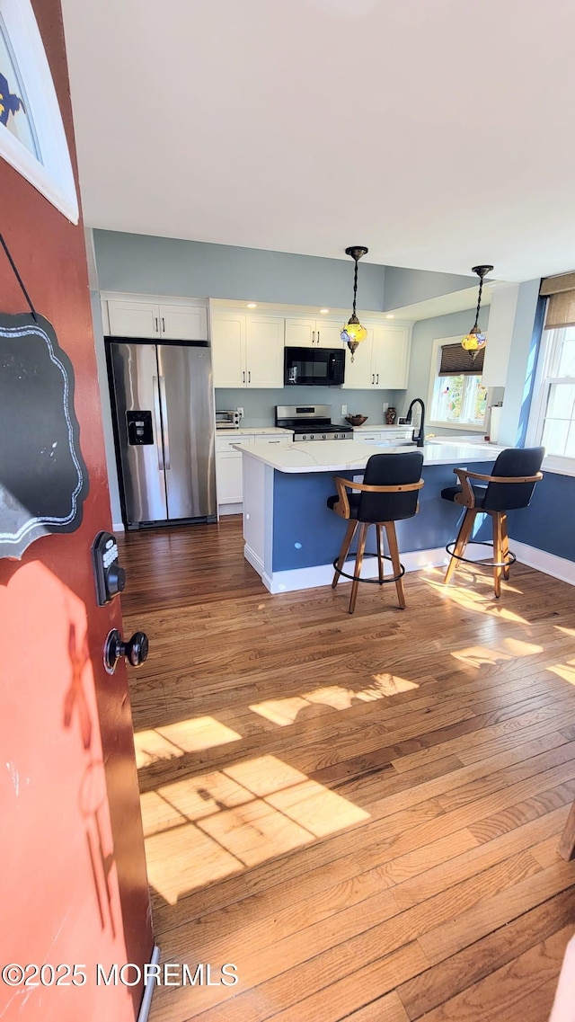 kitchen with stainless steel appliances, hanging light fixtures, light countertops, and white cabinets