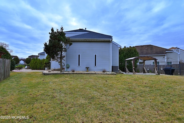 view of side of home with central AC, fence, and a lawn