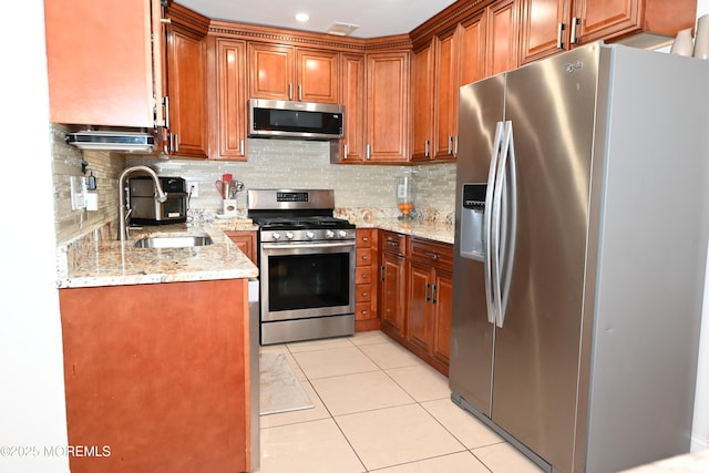 kitchen featuring light tile patterned floors, stainless steel appliances, a sink, backsplash, and brown cabinetry