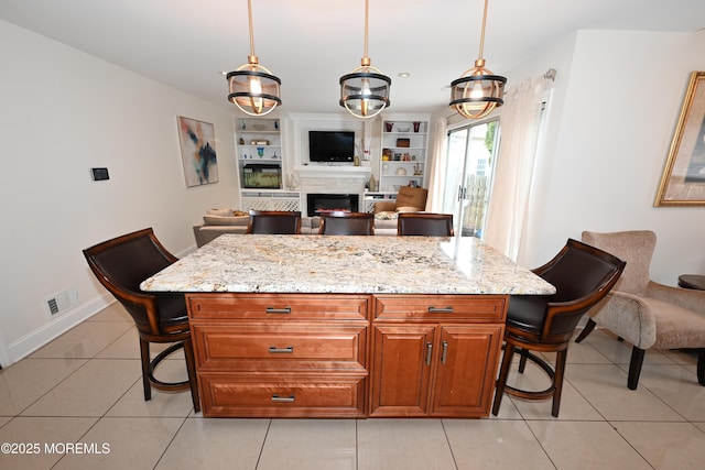 kitchen featuring a warm lit fireplace, hanging light fixtures, a breakfast bar, and light stone countertops