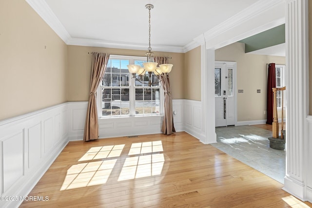 unfurnished dining area featuring a chandelier, a wainscoted wall, visible vents, light wood-style floors, and ornamental molding