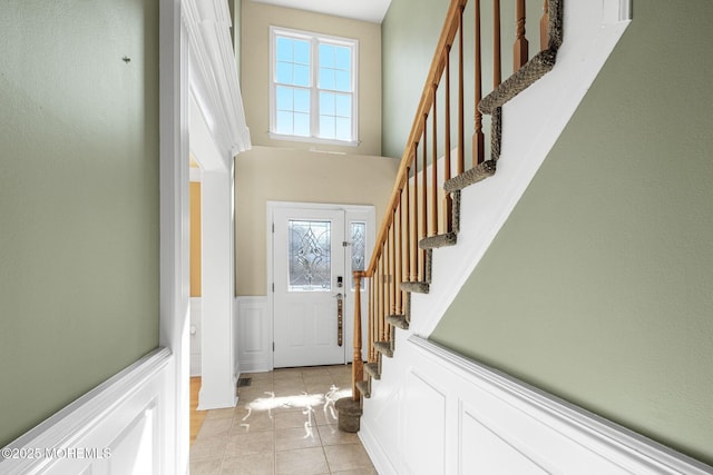 foyer with a wainscoted wall, a high ceiling, light tile patterned floors, and a wealth of natural light