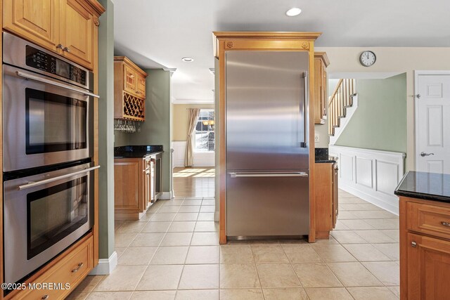 kitchen featuring dark stone counters, wainscoting, appliances with stainless steel finishes, and light tile patterned flooring