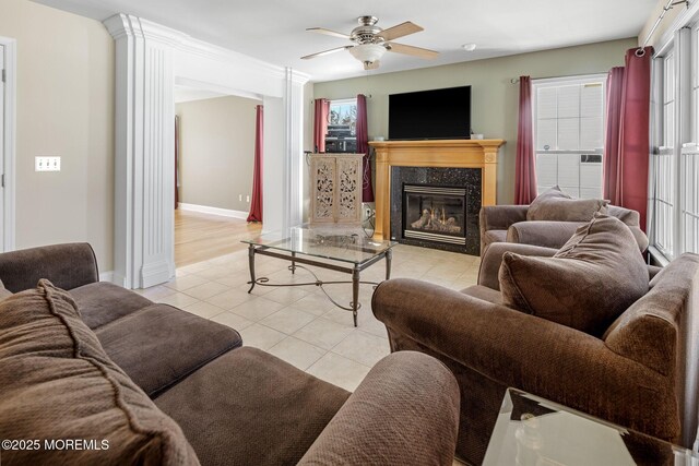 living room with light tile patterned floors, a premium fireplace, a ceiling fan, and baseboards