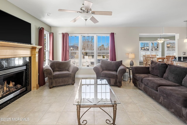 living area with a ceiling fan, a wealth of natural light, light tile patterned floors, and a premium fireplace